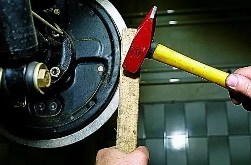 Зняття прикипілого гальмівного барабана: акуратні удари молотком через дерев’яний брусок по краю барабана