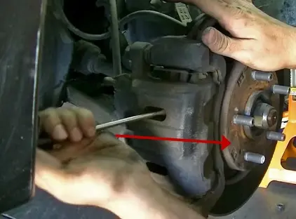 Откручивание болта крепления суппорта дисковых тормозов при ремонте (стрелка)
