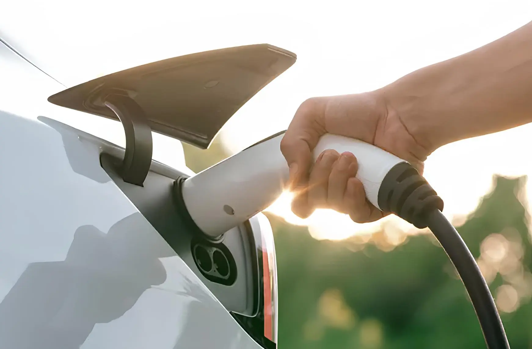 Заряджання електромобіля: рука підключає зарядний кабель до порта, крупний план