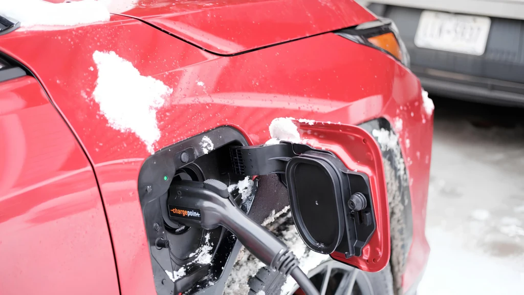 Заряджання електромобіля взимку: червоне авто зі снігом, штекер підключений до зарядного порта