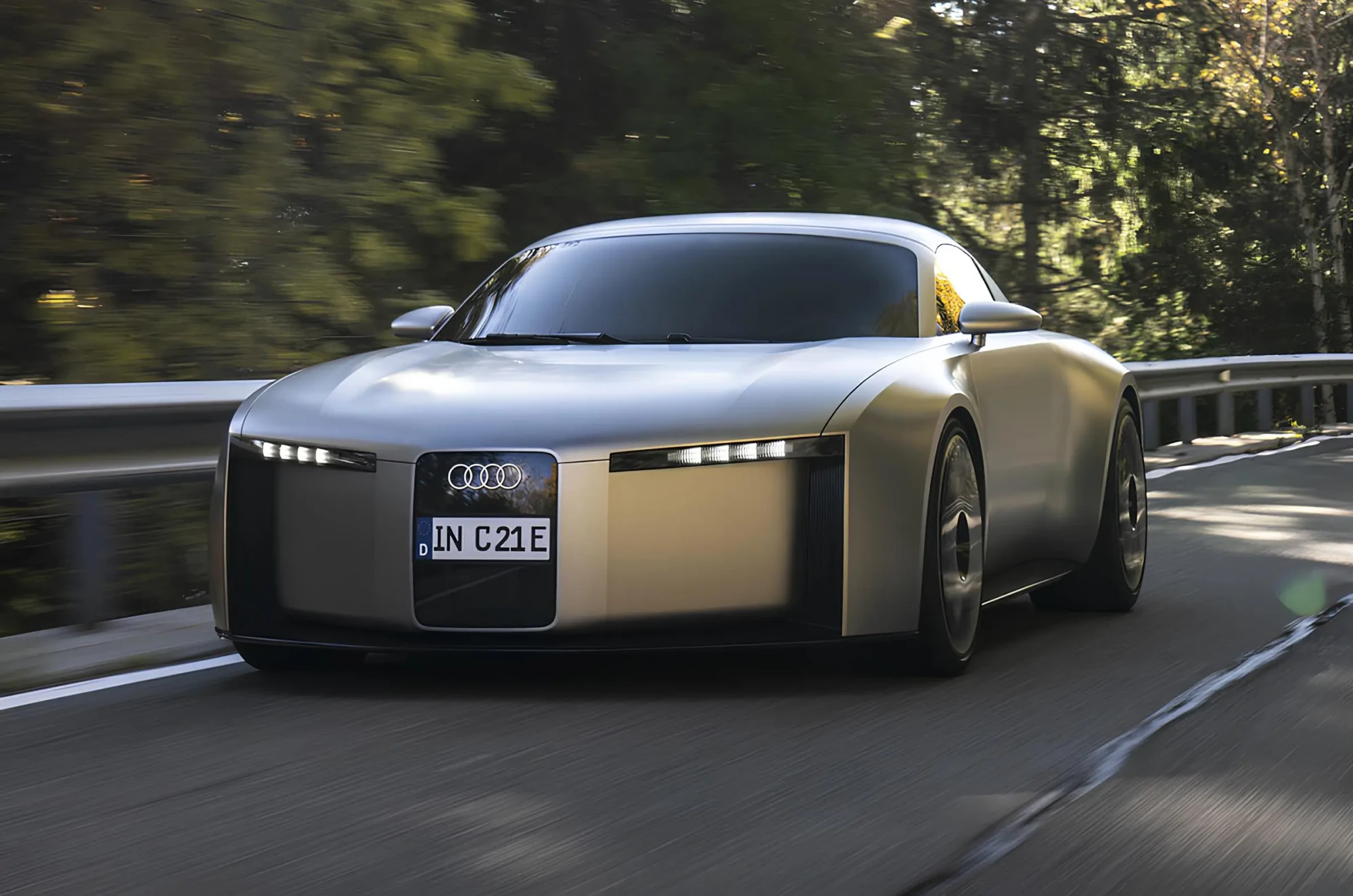 Сріблястий концепт-кар Audi їде звивистою дорогою: фронтальний ракурс, вузькі LED-фари, розмитий ліс і відбійник на тлі.