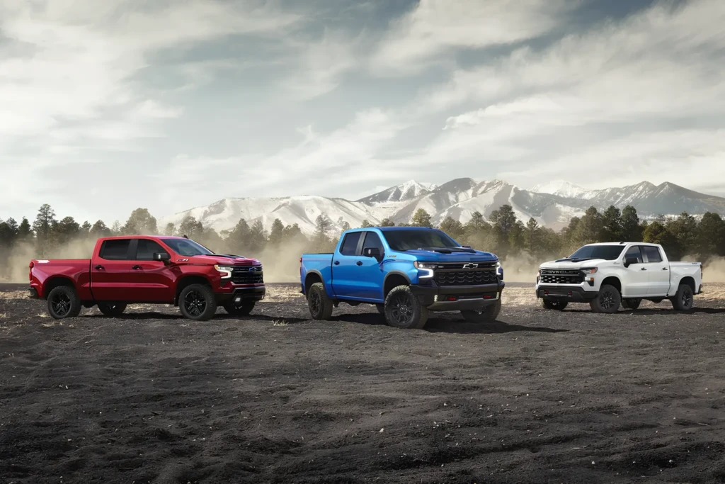 Три пикапа Chevrolet Silverado на бездорожье: красный, синий и белый на фоне гор