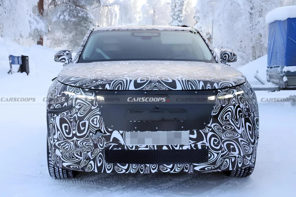 Фронтальный вид замаскированного прототипа кроссовера на зимних тестах: автомобиль в камуфляже, снежная дорога, включённые фары.