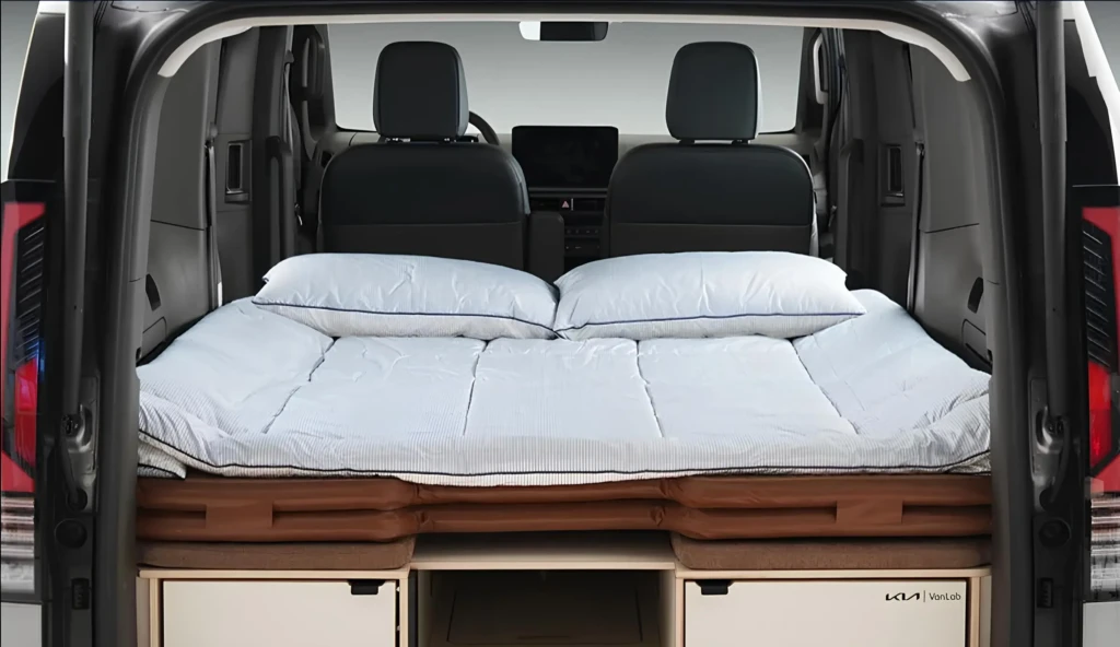 Спальне місце у багажнику Kia VanLab: розкладний матрац із подушками на платформі, під ним — висувні модулі для зберігання.