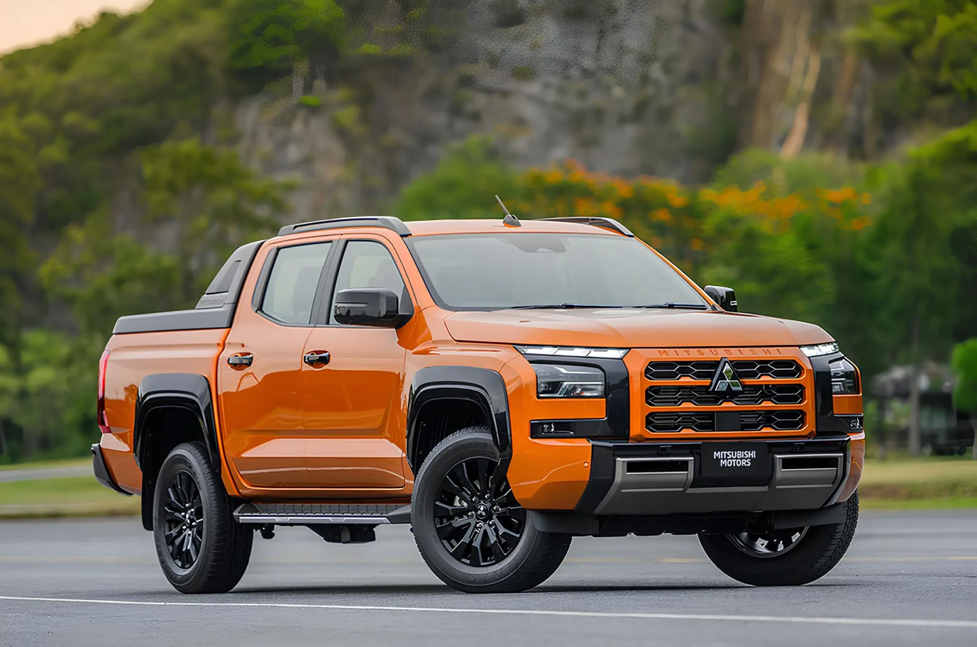 Помаранчевий пікап Mitsubishi на дорозі, вигляд спереду збоку на фоні зелених пагорбів