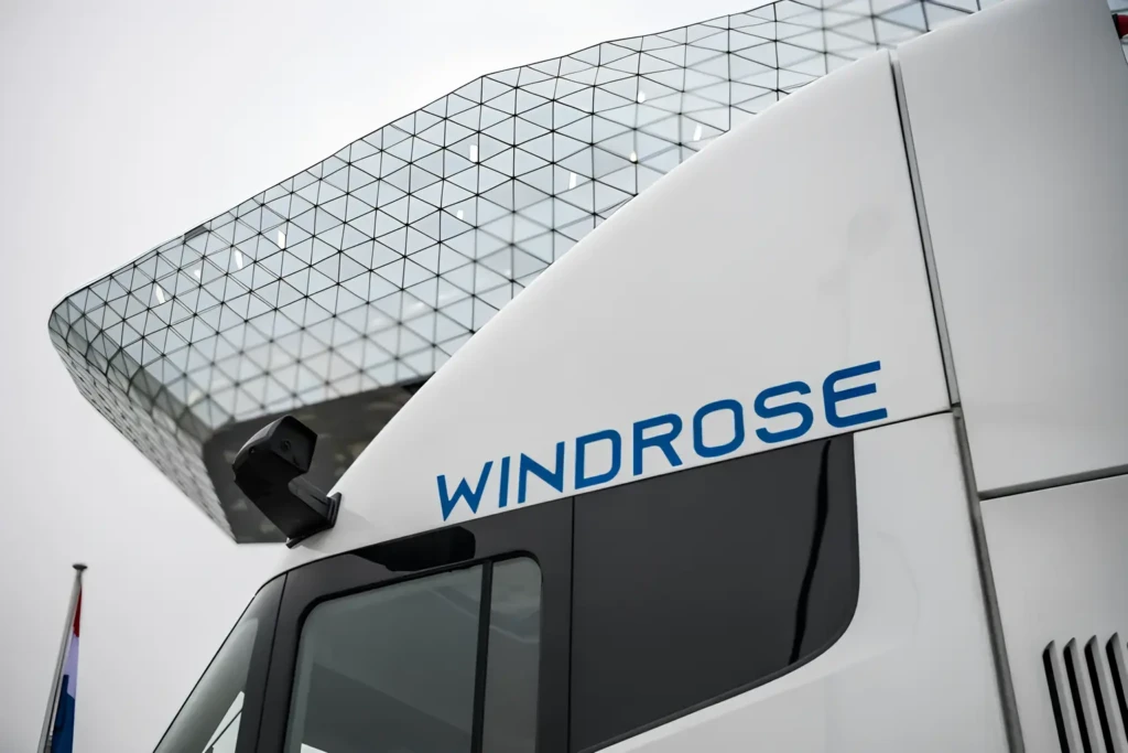 Крупний план кабіни білого електричного тягача з написом WINDROSE на фоні скляного даху будівлі.