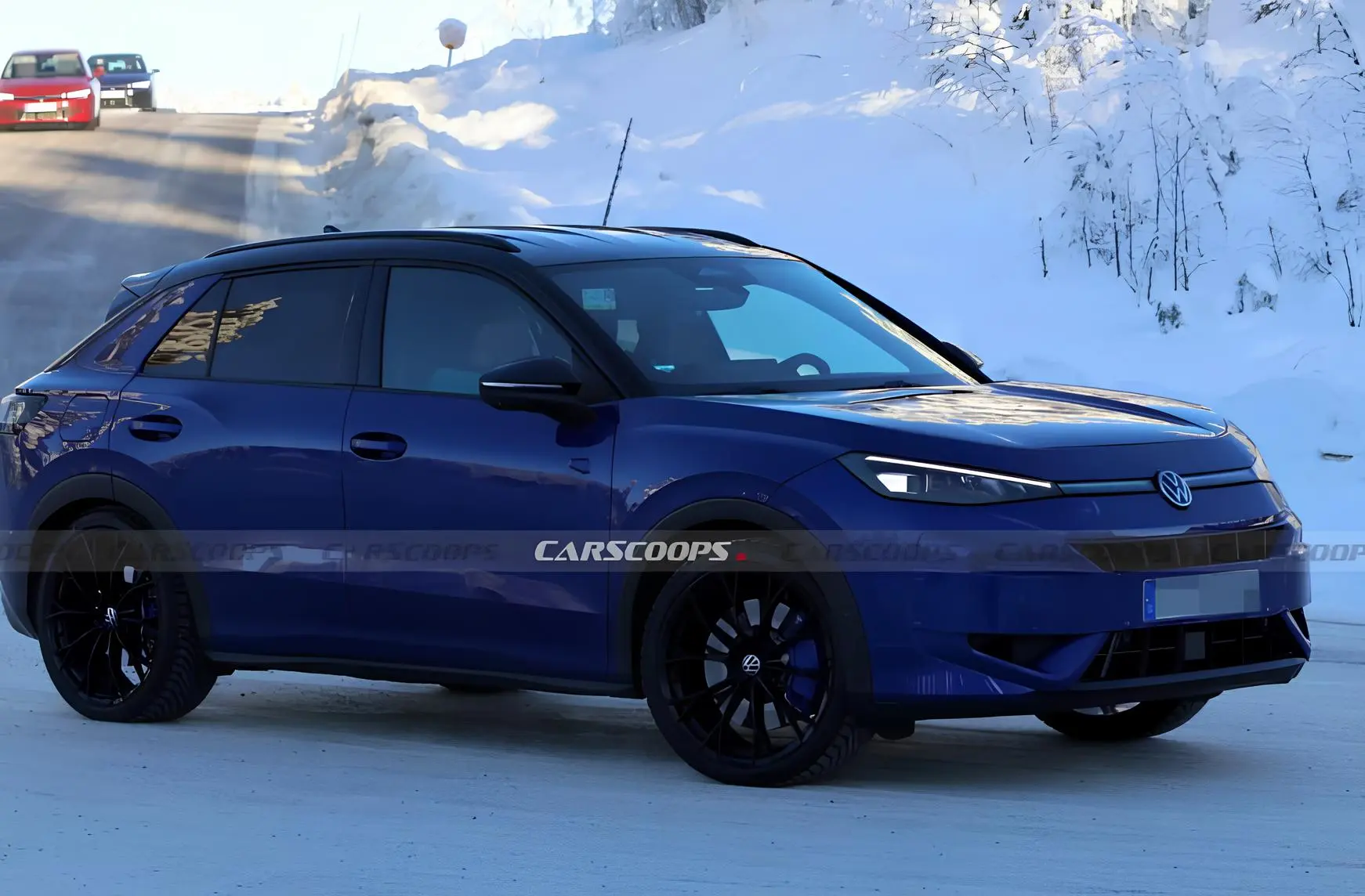 Синій тестовий кросовер Volkswagen на зимовій дорозі: боковий ракурс, чорні диски, снігові замети на фоні.