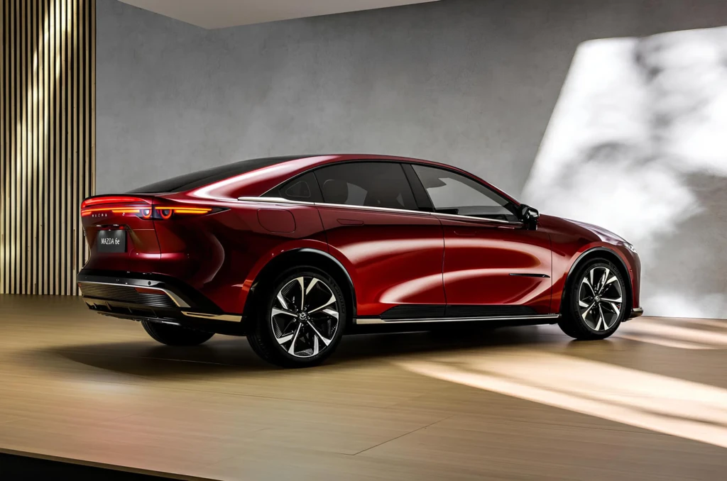 Красный седан Mazda 6e на подиуме: ракурс сзади три четверти, узкие светодиодные фонари и купеобразный силуэт