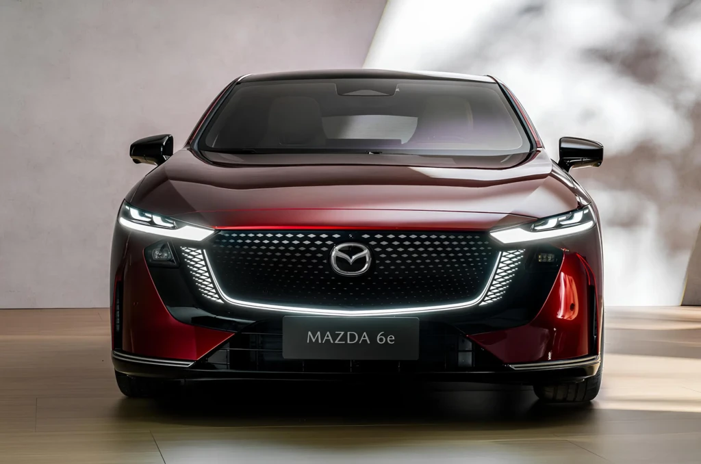 Червоний седан Mazda 6e спереду: велика чорна решітка з підсвіткою, вузькі LED-фари та емблема Mazda по центру Mazda