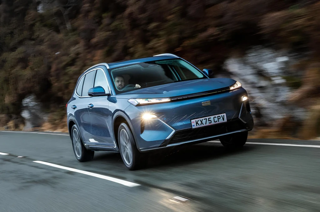 Синій кросовер їде мокрою дорогою, фари увімкнені.