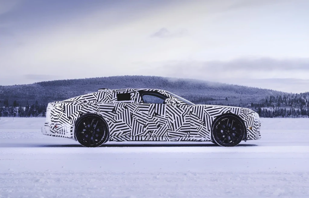 Jaguar GT в камуфляже: боковой профиль на заснеженной трассе, чёрные колёса, зимний лес на фоне