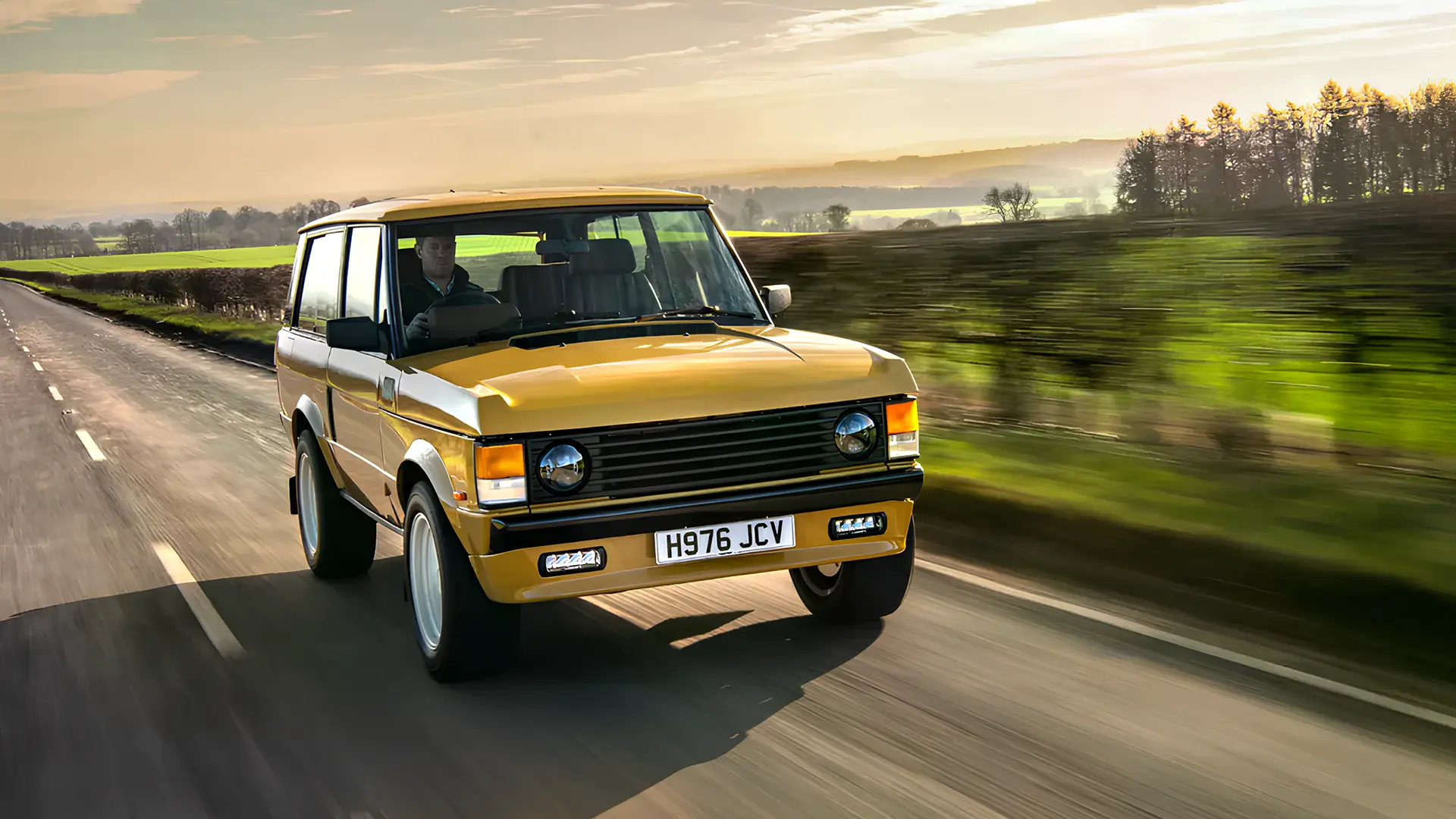 Класичний Range Rover жовтого кольору під час руху заміською дорогою