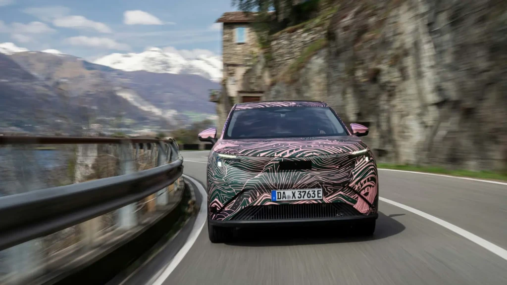 Камуфлированный электрический кроссовер в движении по горной дороге, вид спереди