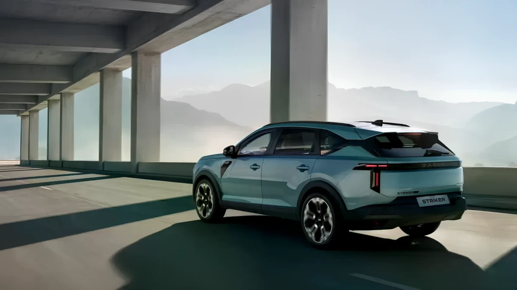 Dacia Striker у русі: вид ззаду 3/4, бірюзовий кросовер їде під естакадою на тлі гір