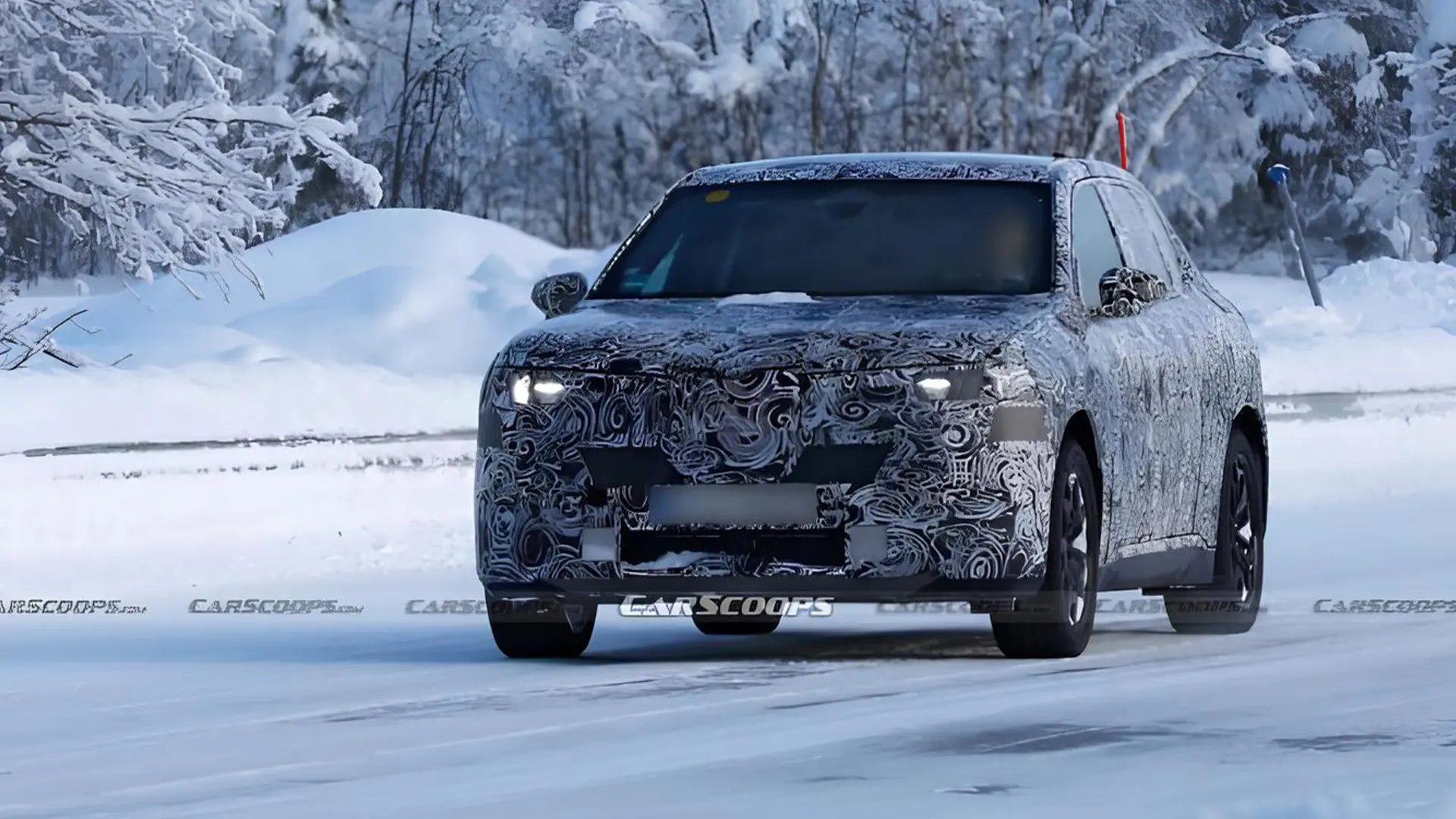 BMW iX1 проходить тестування, прототип кросовера в камуфляжі на зимовій дорозі, вид ззаду збоку