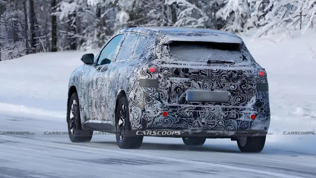 BMW iX1 проходить тестування, прототип кросовера в камуфляжі на зимовій дорозі, вид ззаду збоку