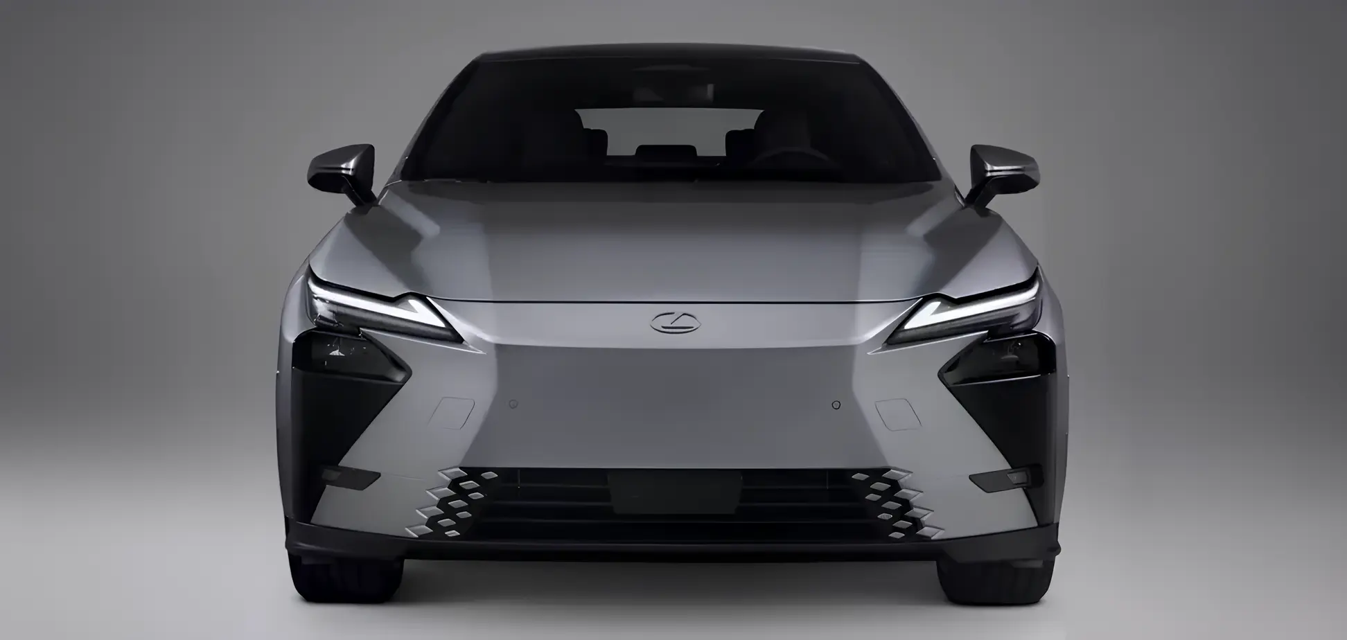 Фронтальний вигляд Lexus ES 350e у сріблястому кольорі: вузькі світлодіодні фари, закритий «електро» ніс без решітки та нижній повітрозабірник з геометричними вставками