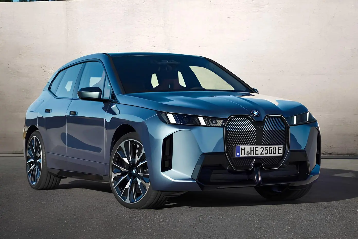 Синій BMW iX на асфальті біля світлої стіни, ракурс спереду під кутом
