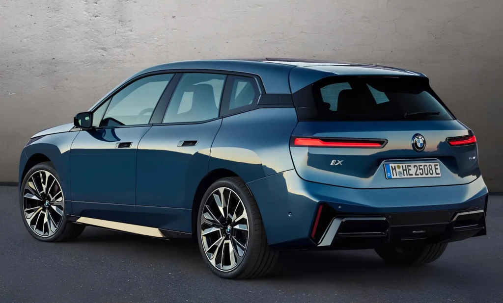 Синій BMW iX, вигляд ззаду під кутом, на асфальті біля сірої стіни