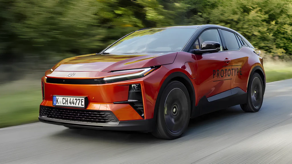 Toyota C-HR+ 2026 помаранчевого кольору в русі, вид спереду збоку