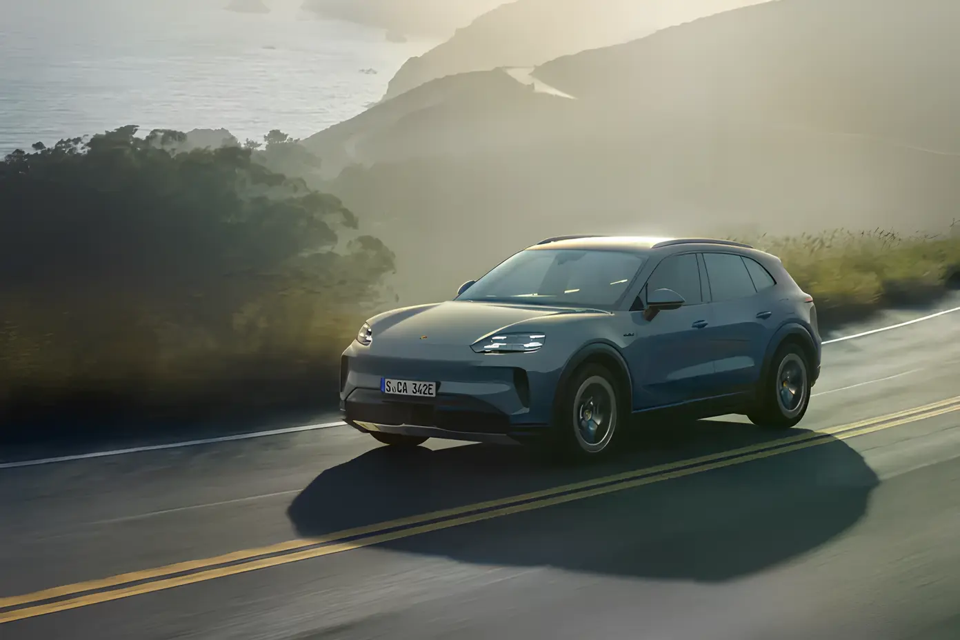 Електричний Porsche Cayenne S на ходу: синій кросовер їде прибережною дорогою у вечірньому тумані