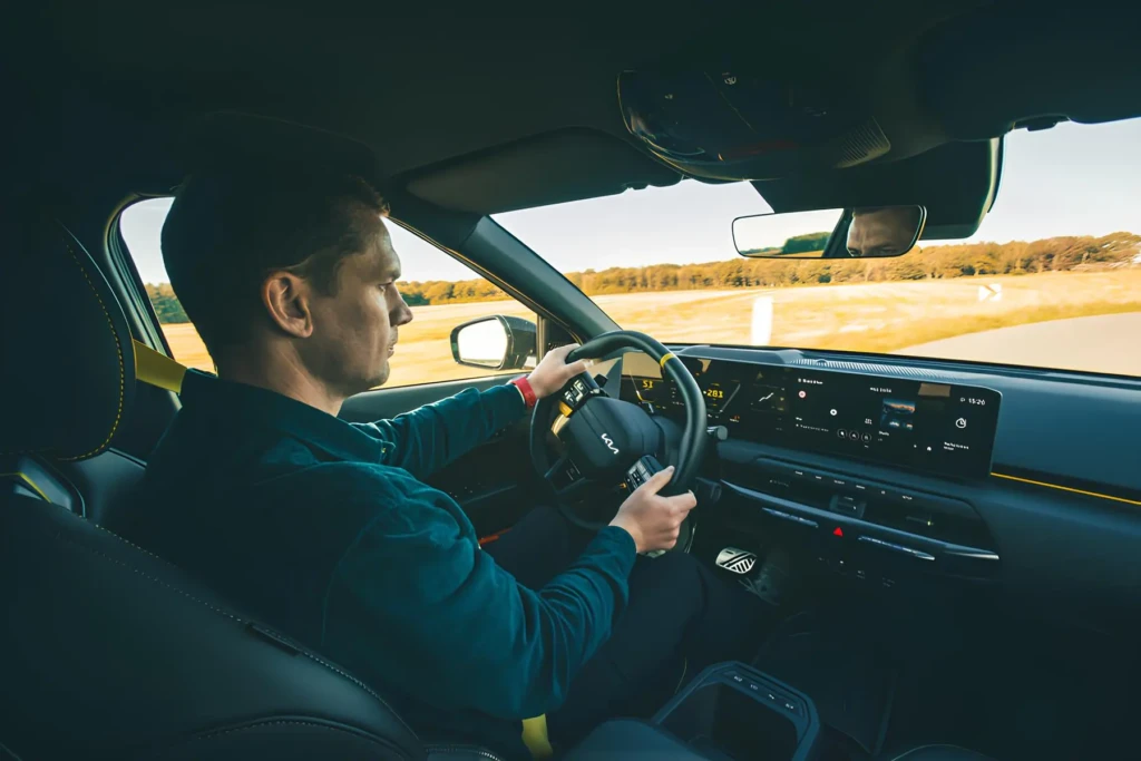Водій за кермом Kia під час тест-драйву на трасі, у салоні широкий цифровий дисплей і сучасна панель приладів