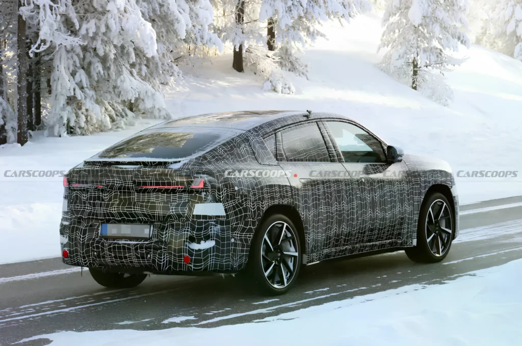 Замаскированный прототип BMW iX4 2027 на зимних тестах, вид сзади сбоку на заснеженной дороге