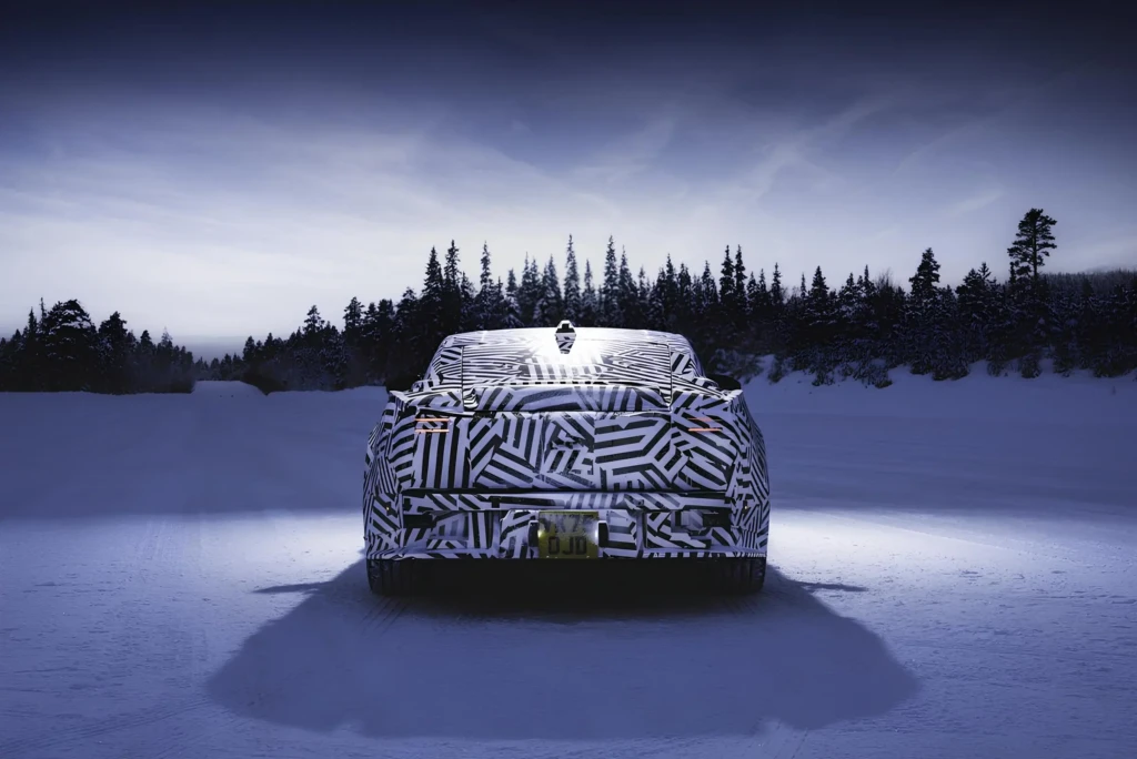 Jaguar GT у камуфляжі на зимових тестах: вигляд ззаду на засніженій трасі, хвойний ліс на горизонті