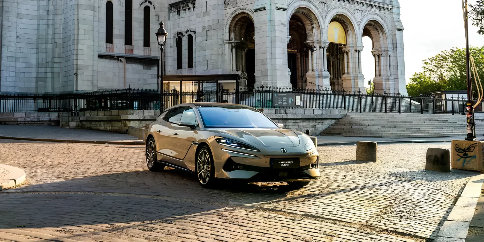 Електричний седан у місті на бруківці біля історичної будівлі з арками, вигляд спереду збоку