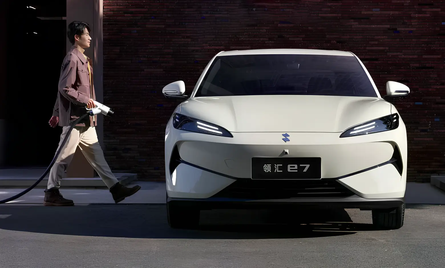 Електроседан BYD Linghui e7 спереду: білий кузов, вузькі LED-фари, чоловік підходить із зарядним пістолетом біля станції