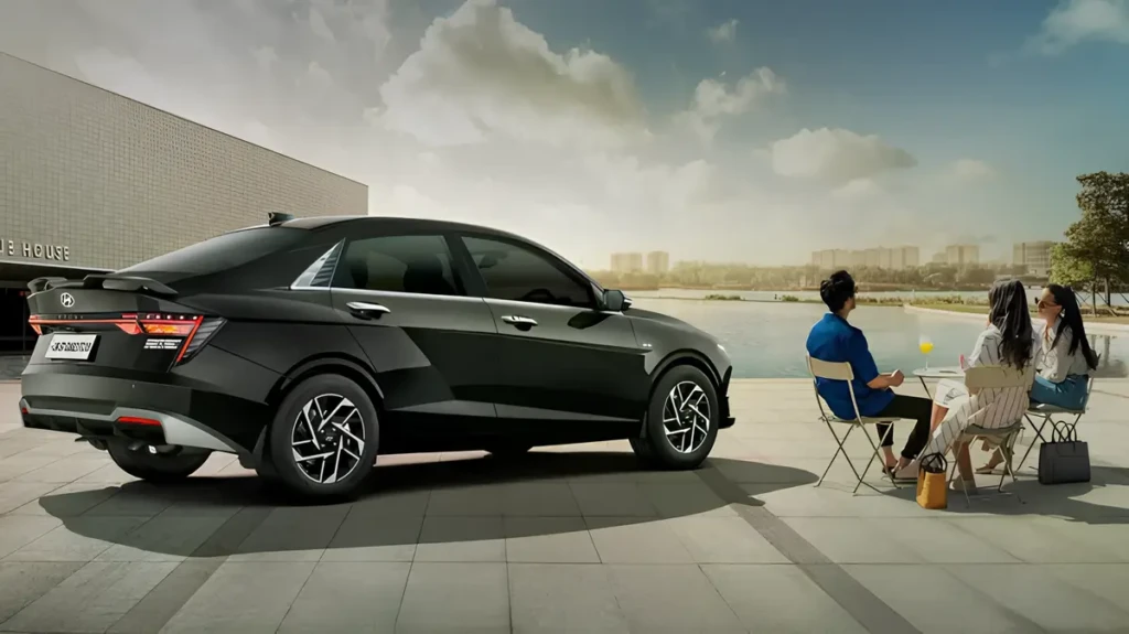 Чёрный Hyundai Accent 2026 сзади-сбоку на набережной; рядом трое людей сидят за столиком у воды