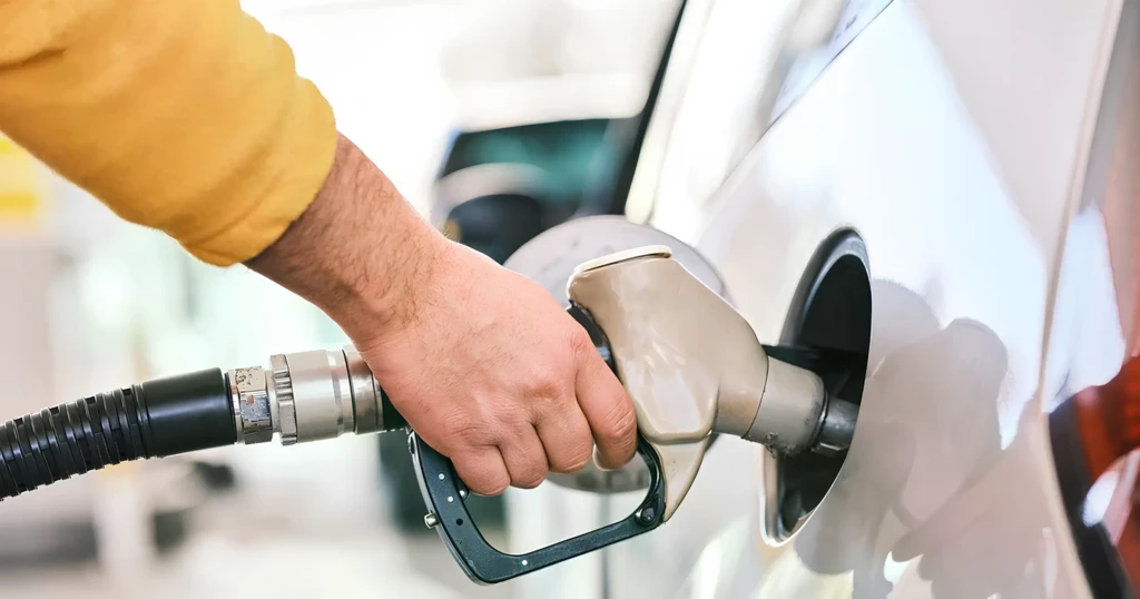 Заправний пістолет у руках водія: заправка автомобіля паливом на АЗС, крупний план горловини бака