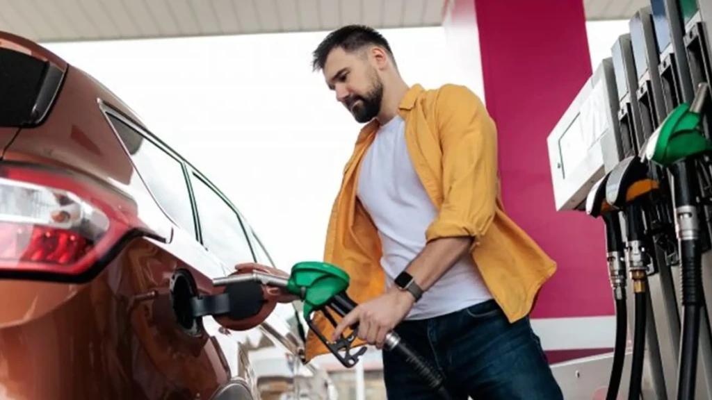 Чоловік заправляє автомобіль на АЗС, тримаючи паливний пістолет