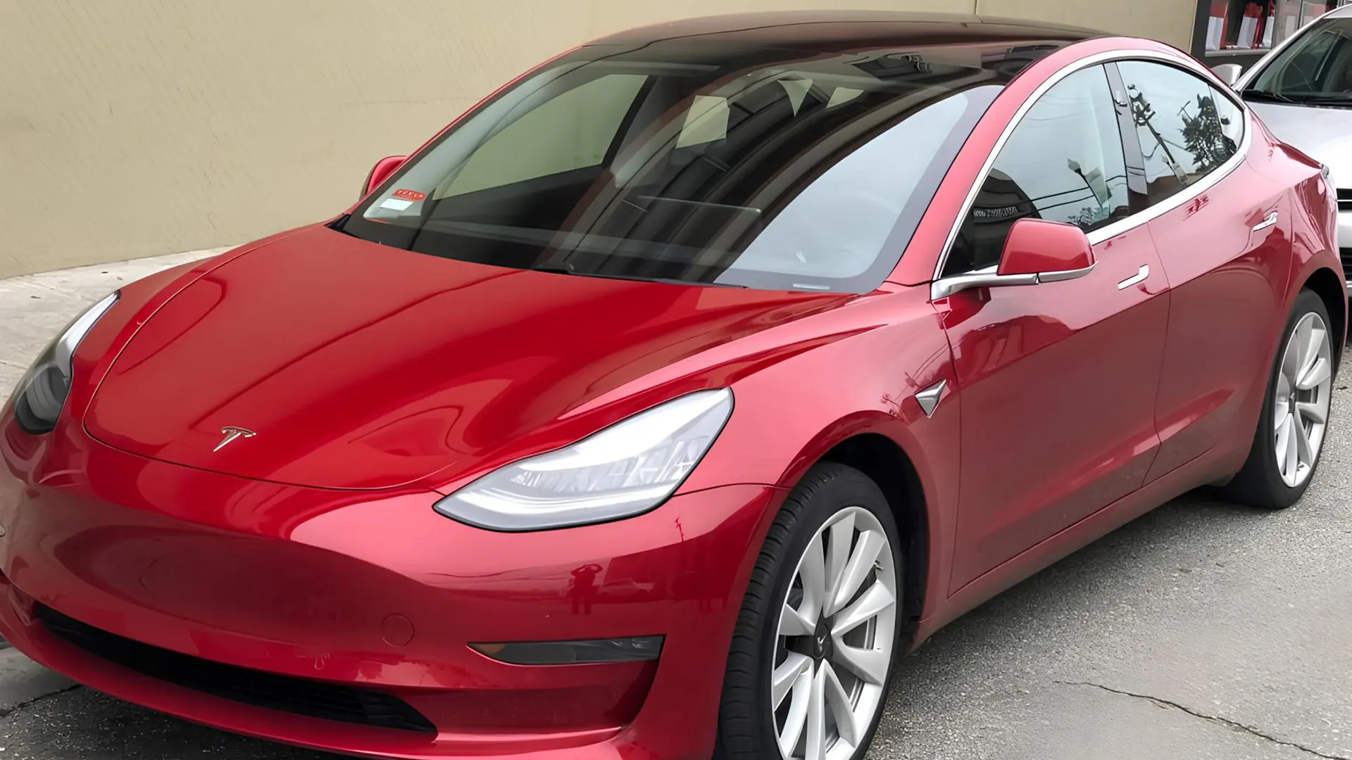 Червоний електромобіль Tesla Model 3, вид спереду збоку на парковці