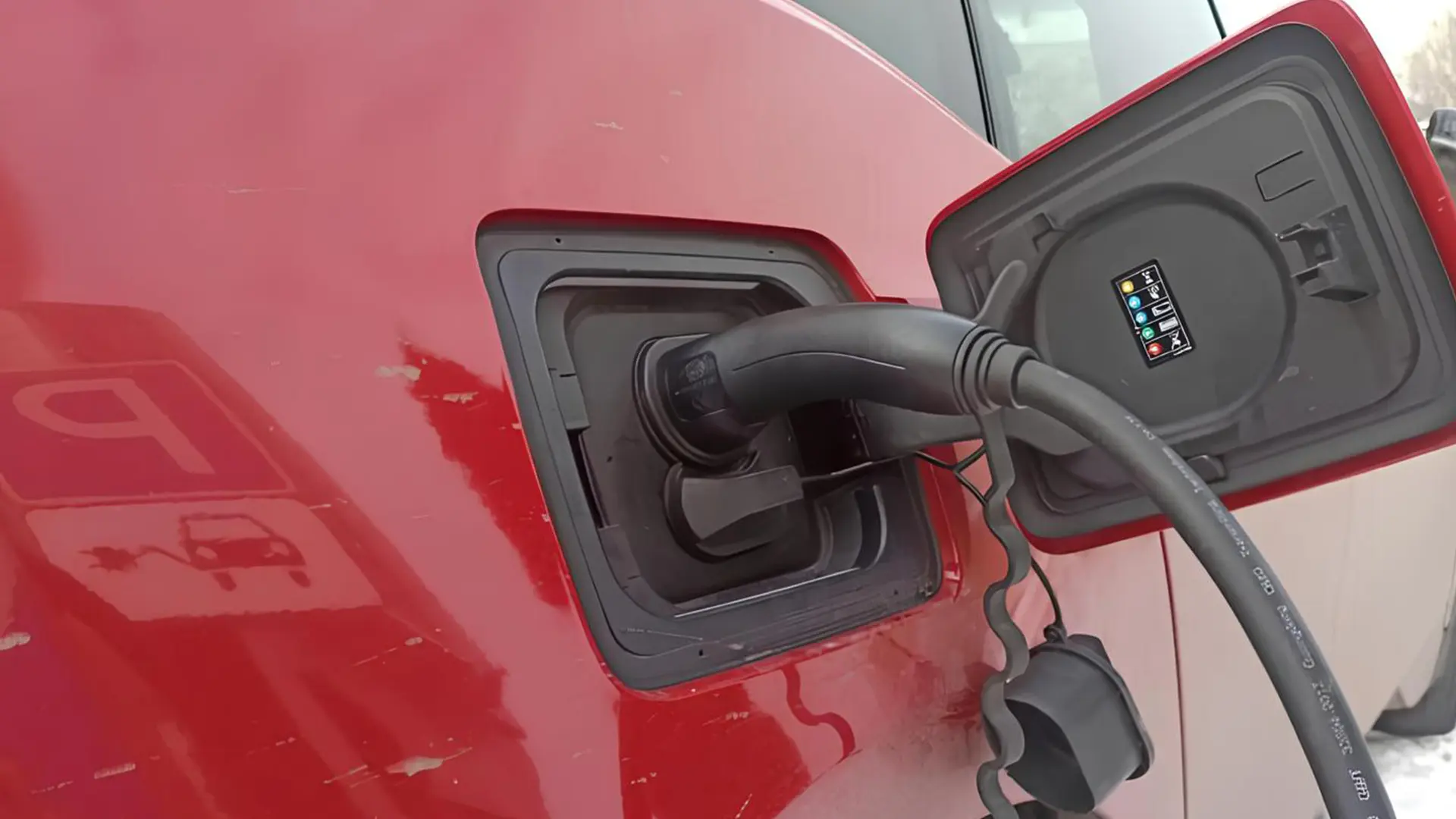 Електромобіль червоного кольору підключений до зарядної станції під час заряджання акумулятора