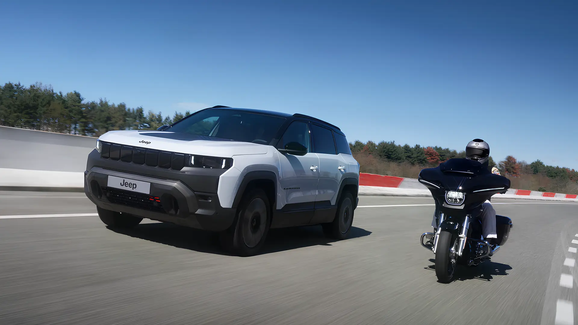 Білий Jeep їде поруч із мотоциклом Harley-Davidson на швидкісній трасі