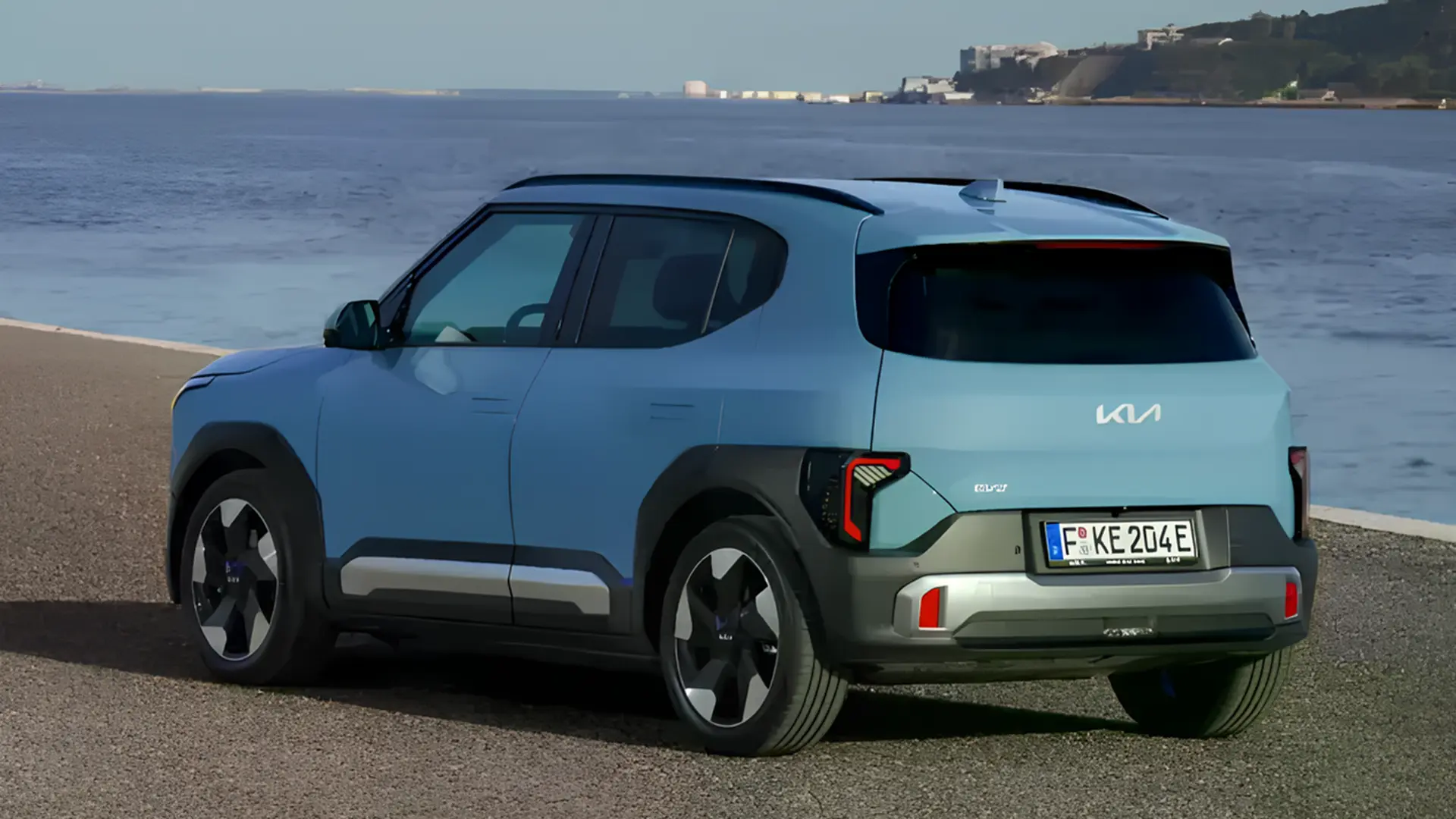 Електричний кросовер Kia блакитного кольору, вид ззаду збоку на тлі узбережжя