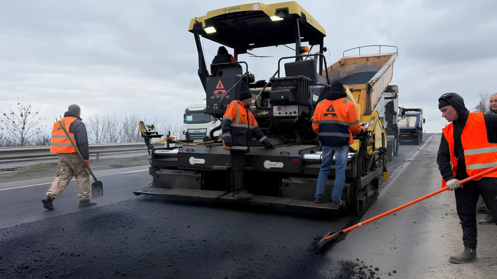 Дорожні працівники укладають новий шар асфальту на автомобільній дорозі за допомогою спецтехніки