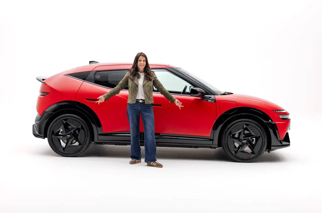 Жінка стоїть біля червоного електромобіля Hyundai Ioniq 3 на студійному фоні