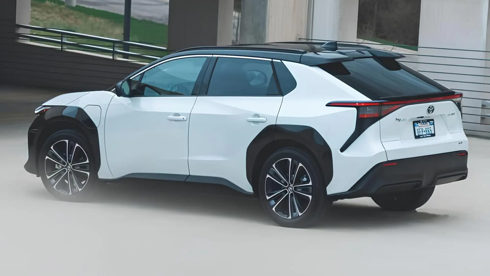 Білий електричний кросовер Toyota bZ4X у русі біля сучасної будівлі
