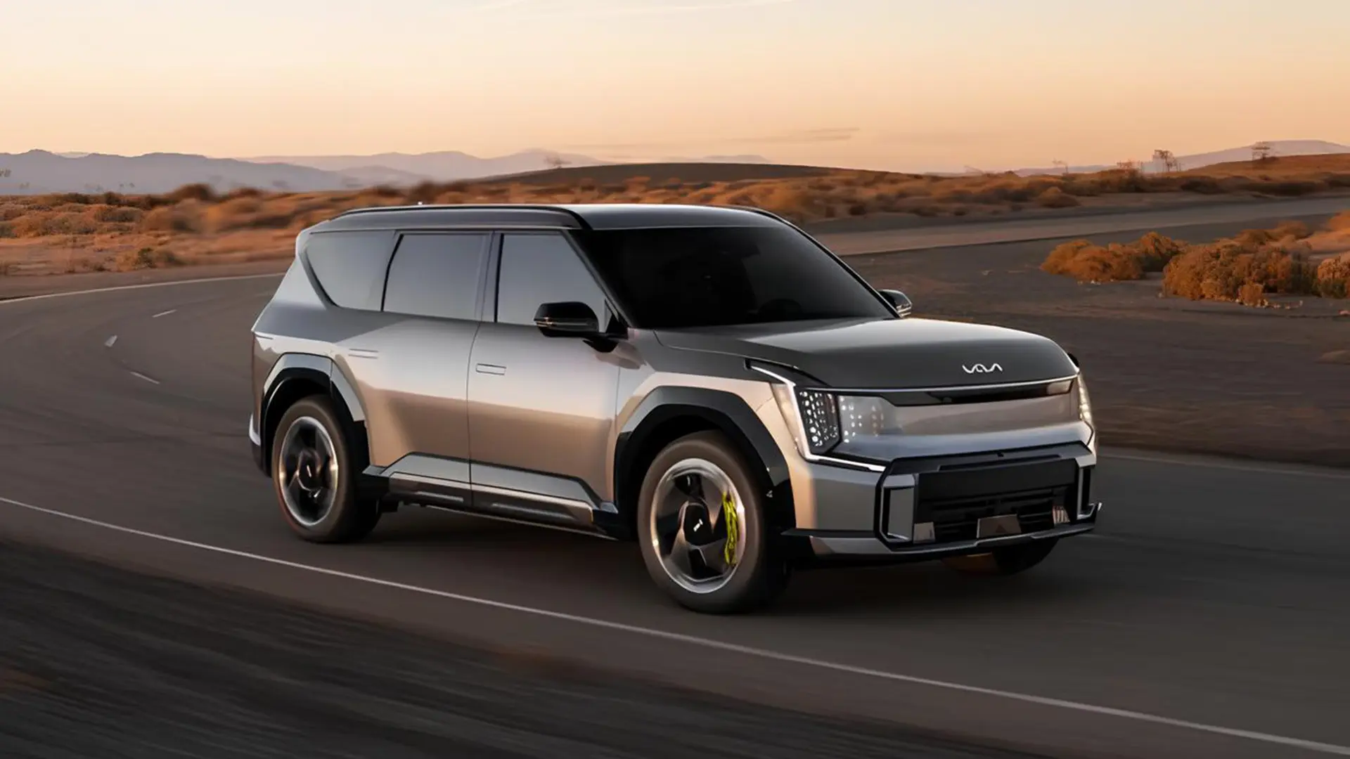 Електричний кросовер Kia EV9 сріблястого кольору рухається дорогою на тлі пустельного пейзажу