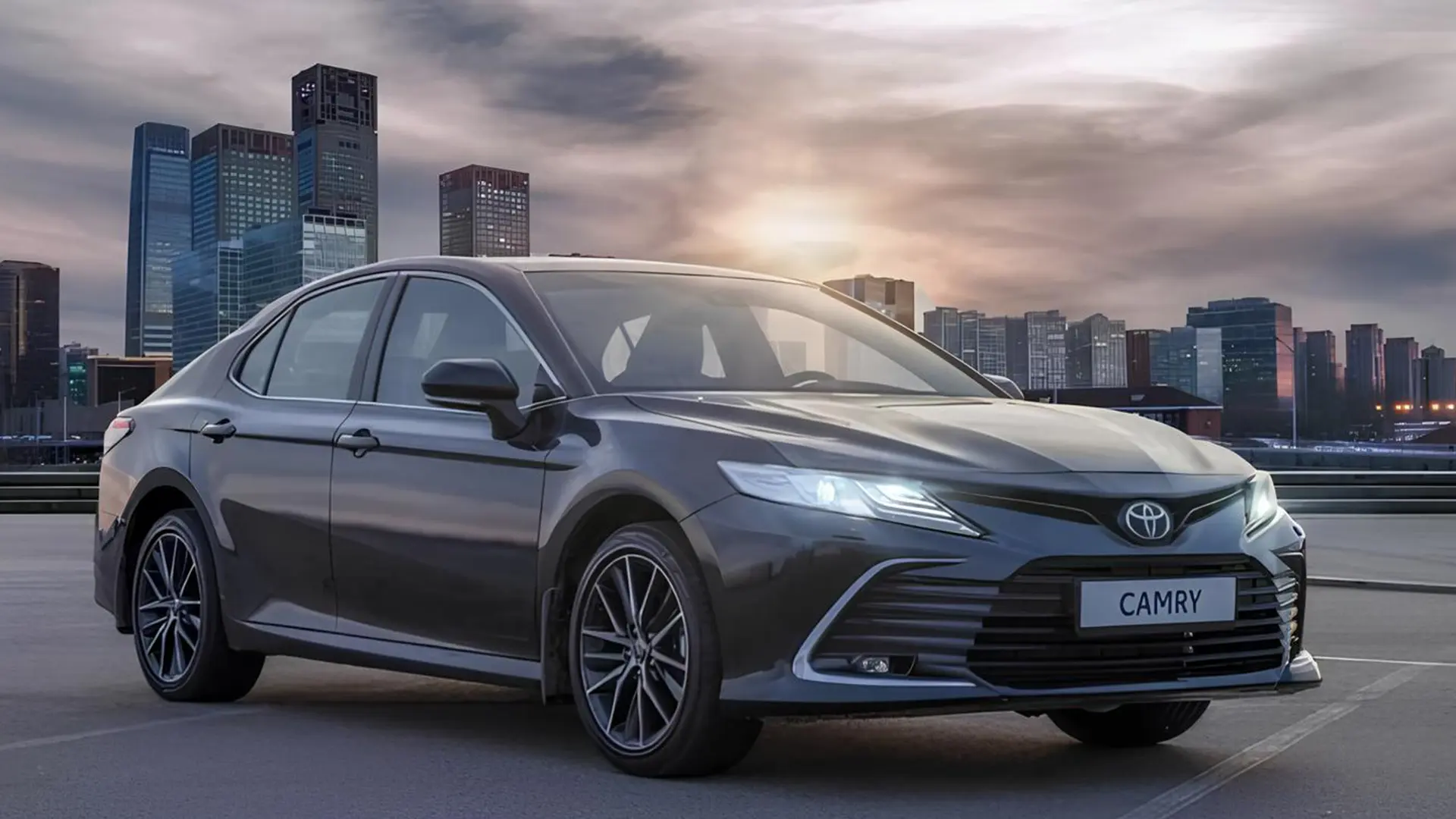 Сіра Toyota Camry XV70 на дорозі на тлі міських будівель
